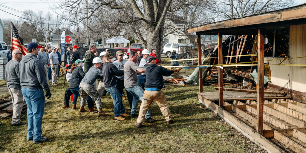 volunteers and neighbors work together to pull down a house, thus displaying catastrophe compassion in action.